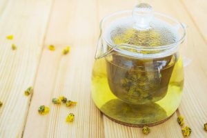 Glass teapot brewing chrysanthemum tea on wooden table.