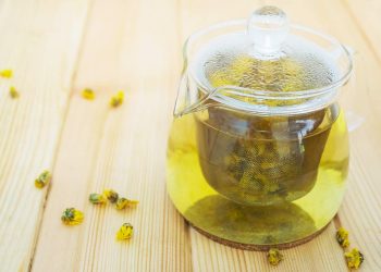 Glass teapot brewing chrysanthemum tea on wooden table.