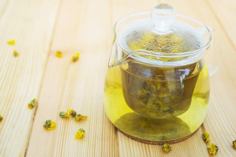 Glass teapot brewing chrysanthemum tea on wooden table.