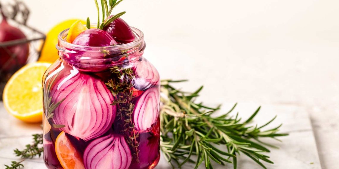 Pickled red onions in a jar with rosemary and lemon slices.