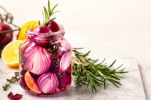 Pickled red onions in a jar with rosemary and lemon slices.