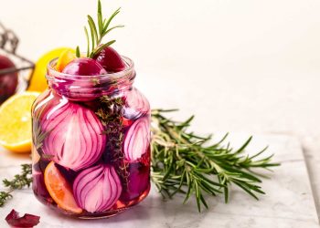 Pickled red onions in a jar with rosemary and lemon slices.