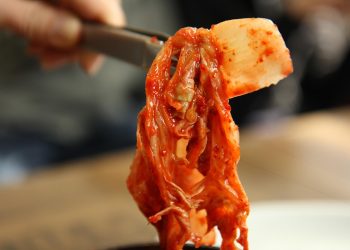 Kimchi held with chopsticks, displaying vibrant colors and texture.