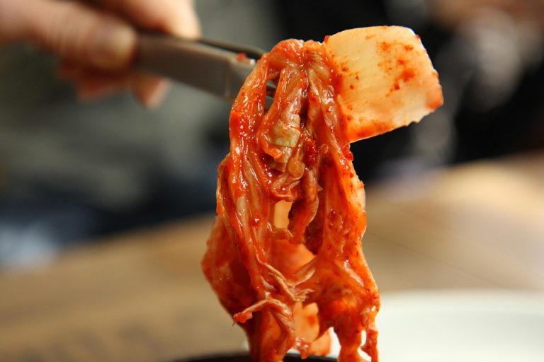 Kimchi held with chopsticks, displaying vibrant colors and texture.
