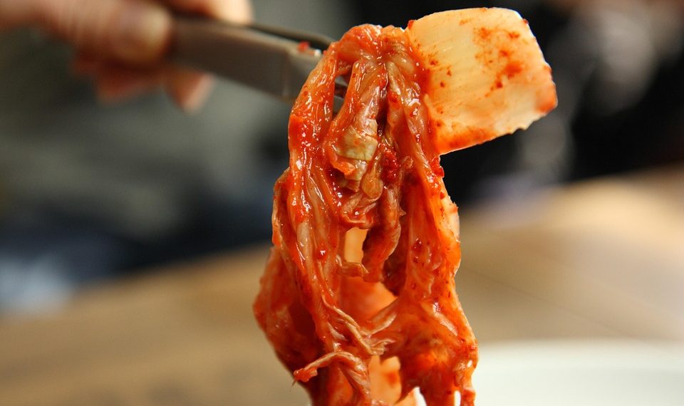 Kimchi held with chopsticks, displaying vibrant colors and texture.