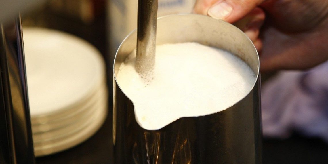 Foaming milk in a metal pitcher for cappuccino preparation.