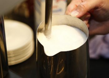 Foaming milk in a metal pitcher for cappuccino preparation.