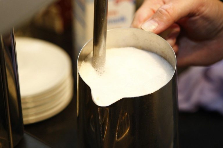 Foaming milk in a metal pitcher for cappuccino preparation.