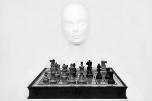 Chess pieces arranged on a board with a mannequin head in the background.