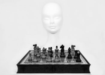 Chess pieces arranged on a board with a mannequin head in the background.