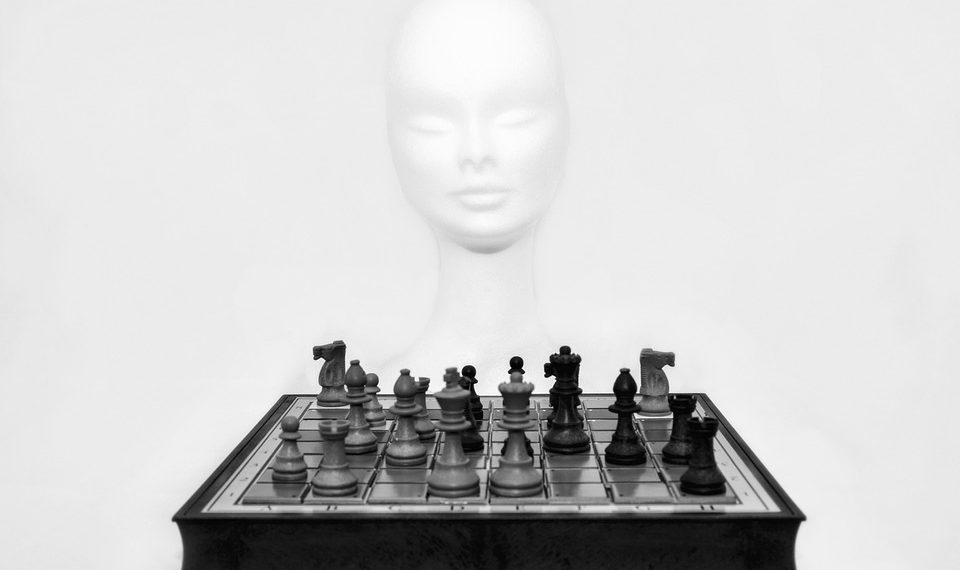 Chess pieces arranged on a board with a mannequin head in the background.
