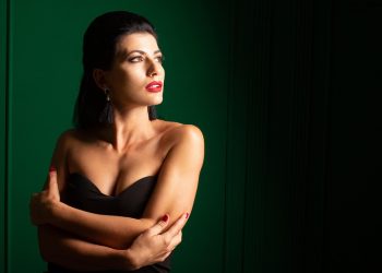 Woman in elegant black dress with red lipstick against green background.