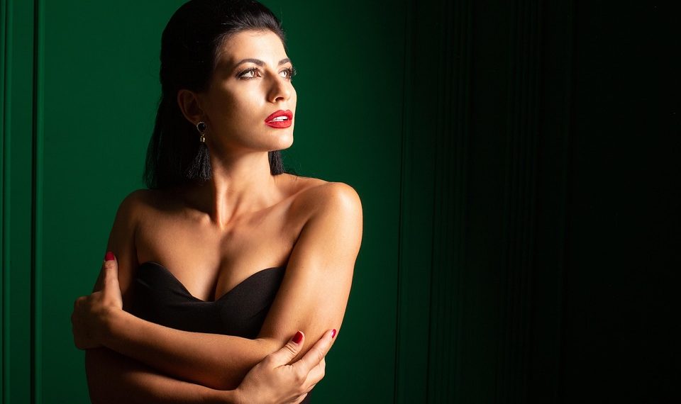 Woman in elegant black dress with red lipstick against green background.