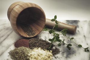 Wooden mortar with pestle, herbs, and spices on a marble surface.