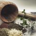 Wooden mortar with pestle, herbs, and spices on a marble surface.