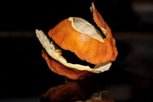 Dry orange peel curls resting on a reflective surface.