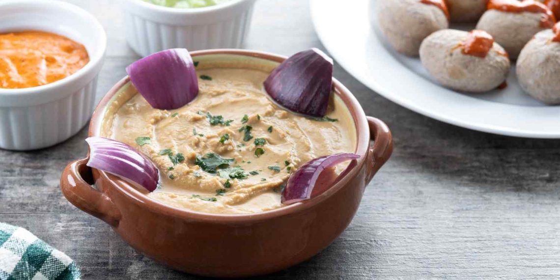 Creamy hummus garnished with red onions and herbs, accompanied by small dipping bowls.