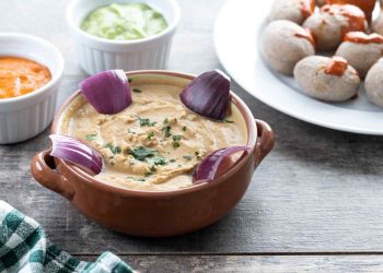 Creamy hummus garnished with red onions and herbs, accompanied by small dipping bowls.