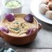 Creamy hummus garnished with red onions and herbs, accompanied by small dipping bowls.