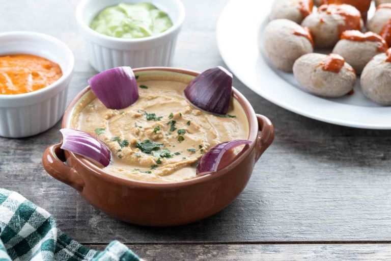 Creamy hummus garnished with red onions and herbs, accompanied by small dipping bowls.