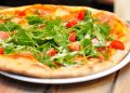 Arugula and tomato pizza garnished with parmesan on a wooden table.