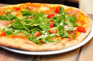 Arugula and tomato pizza garnished with parmesan on a wooden table.