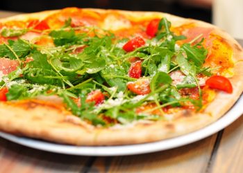 Arugula and tomato pizza garnished with parmesan on a wooden table.