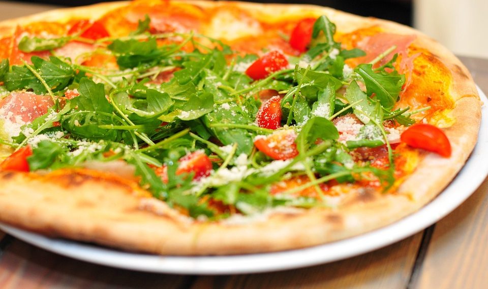 Arugula and tomato pizza garnished with parmesan on a wooden table.