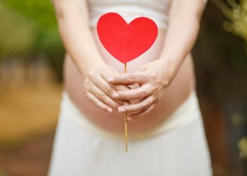 Pregnant woman holding a red heart cutout over her belly.