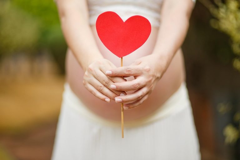 Pregnant woman holding a red heart cutout over her belly.