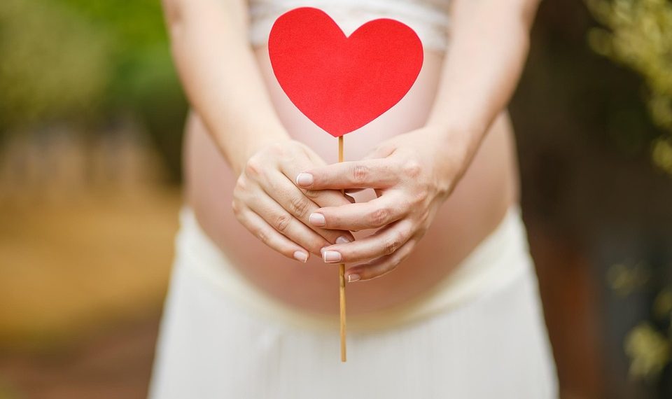 Pregnant woman holding a red heart cutout over her belly.