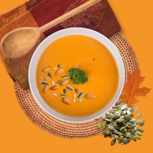 Creamy pumpkin soup garnished with seeds and herbs on an autumn-themed setup.