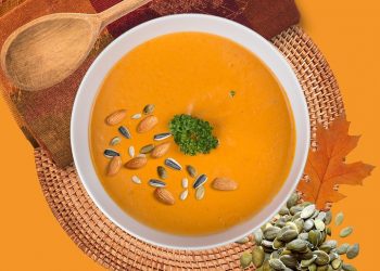 Creamy pumpkin soup garnished with seeds and herbs on an autumn-themed setup.