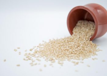 Brown rice spilling from a clay pot onto a white surface.