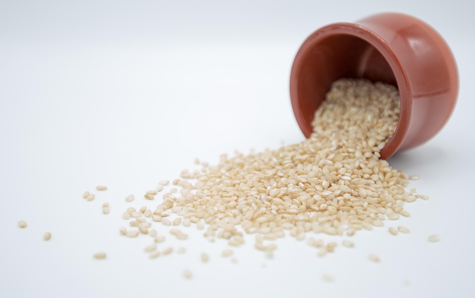 Brown rice spilling from a clay pot onto a white surface.