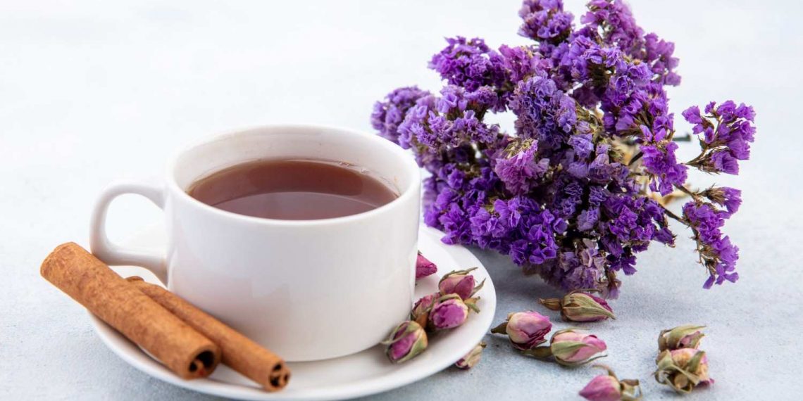 Tea cup with cinnamon sticks and purple flowers on a white plate.