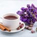 Tea cup with cinnamon sticks and purple flowers on a white plate.
