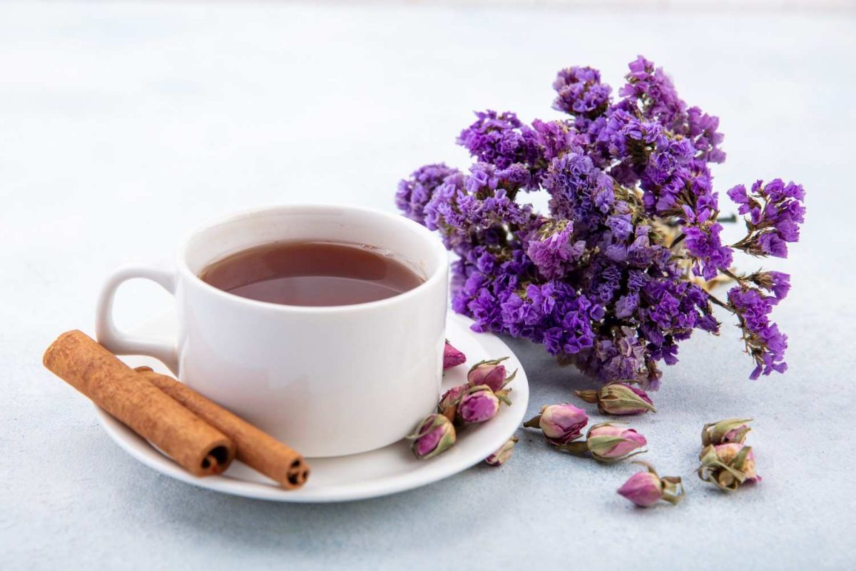 Tea cup with cinnamon sticks and purple flowers on a white plate.