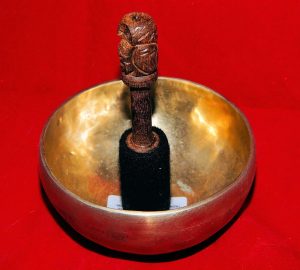 Tibetan singing bowl with a wooden mallet on a red background.