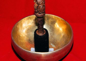 Tibetan singing bowl with a wooden mallet on a red background.