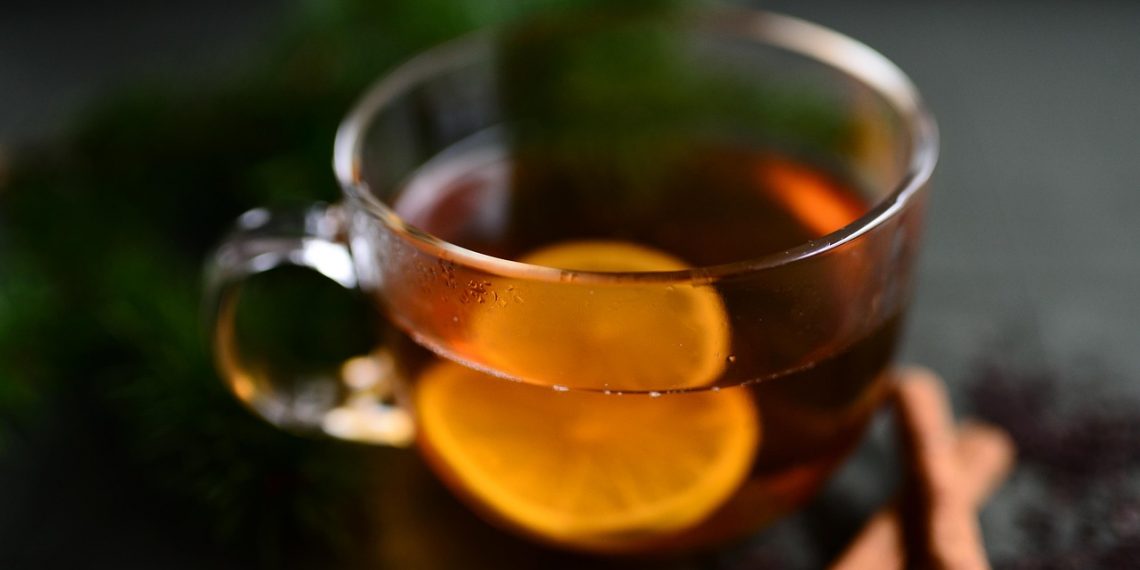 Hot lemon tea in a glass cup with cinnamon sticks.