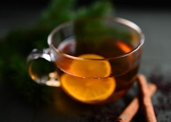 Hot lemon tea in a glass cup with cinnamon sticks.