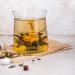 Blooming tea flower in a glass with sugar cubes and herbs scattered around.