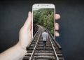 Person walking on train tracks emerging from phone.