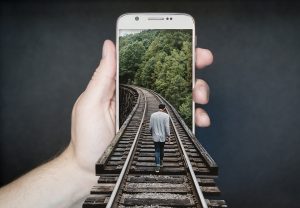 Person walking on train tracks emerging from phone.