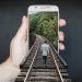 Person walking on train tracks emerging from phone.
