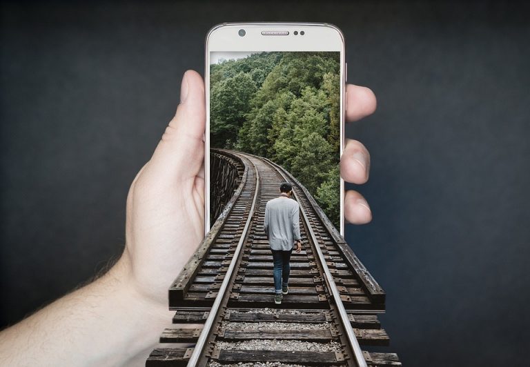 Person walking on train tracks emerging from phone.