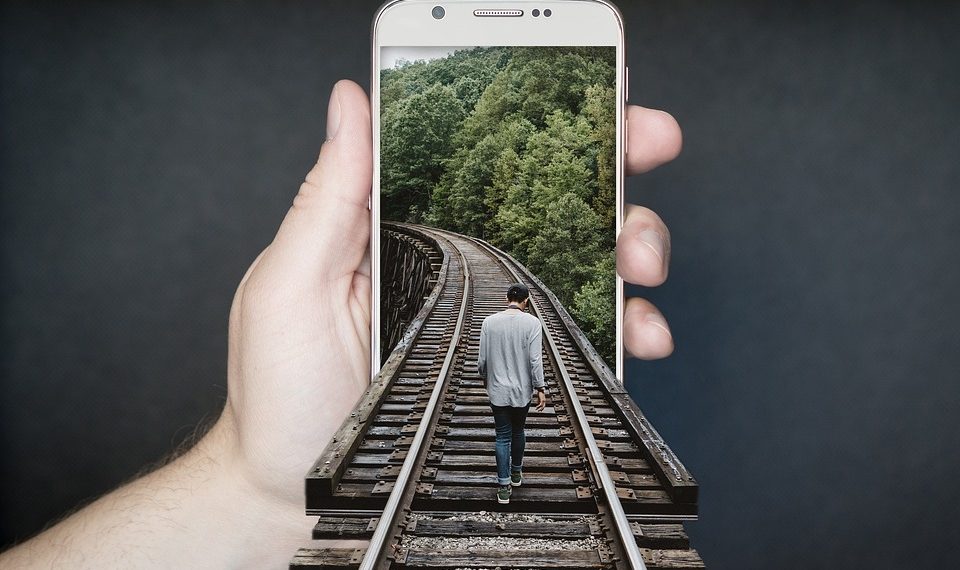 Person walking on train tracks emerging from phone.