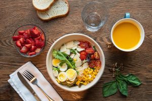 Healthy salad with eggs, corn, and tomatoes next to strawberries and orange juice.
