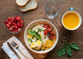Healthy salad with eggs, corn, and tomatoes next to strawberries and orange juice.